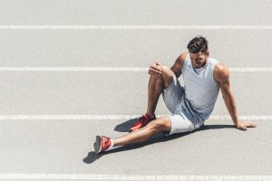 fit young jogger with leg injury sitting on running track